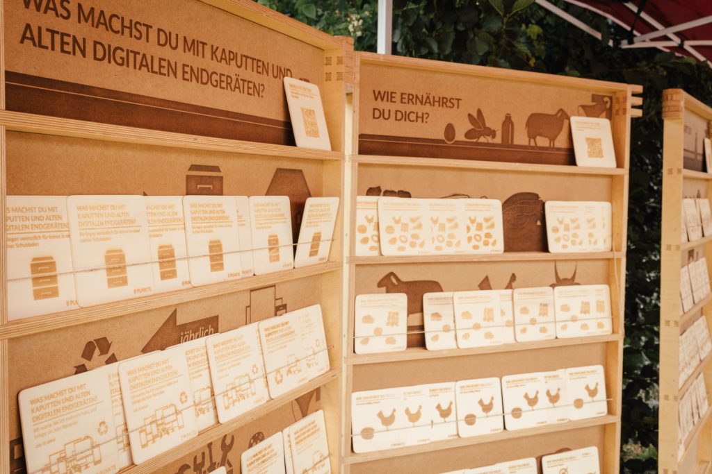 Mobile Holzregalelemente mit herausnehmbaren Holztafeln. Es gibt Themen wie z.B. "Wie ernährst du dich?" oder "Was machst du mit kaputten und alten digitalen Endgeräten?".