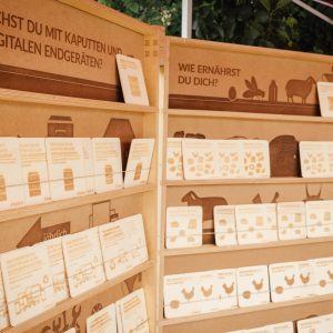 Mobile Holzregalelemente mit herausnehmbaren Holztafeln. Es gibt Themen wie z.B. "Wie ernährst du dich?" oder "Was machst du mit kaputten und alten digitalen Endgeräten?".